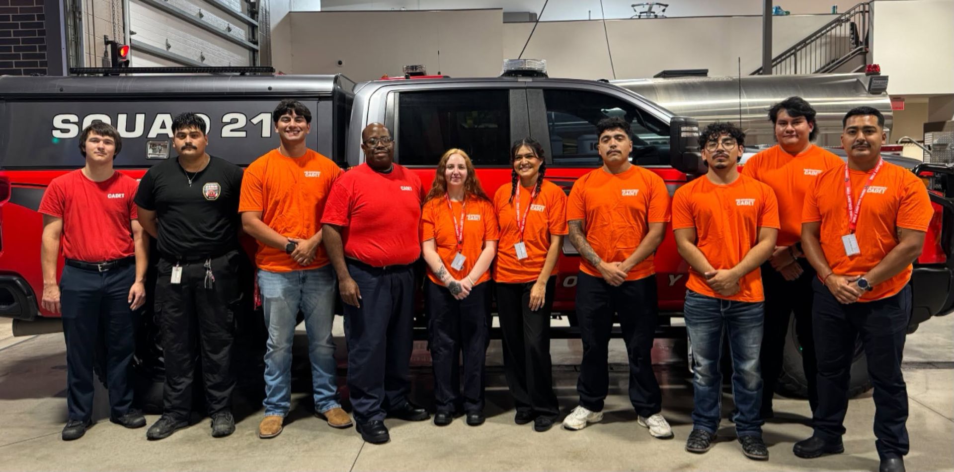 Group of workers in orange and black uniforms posing in front of a large truck in a garage