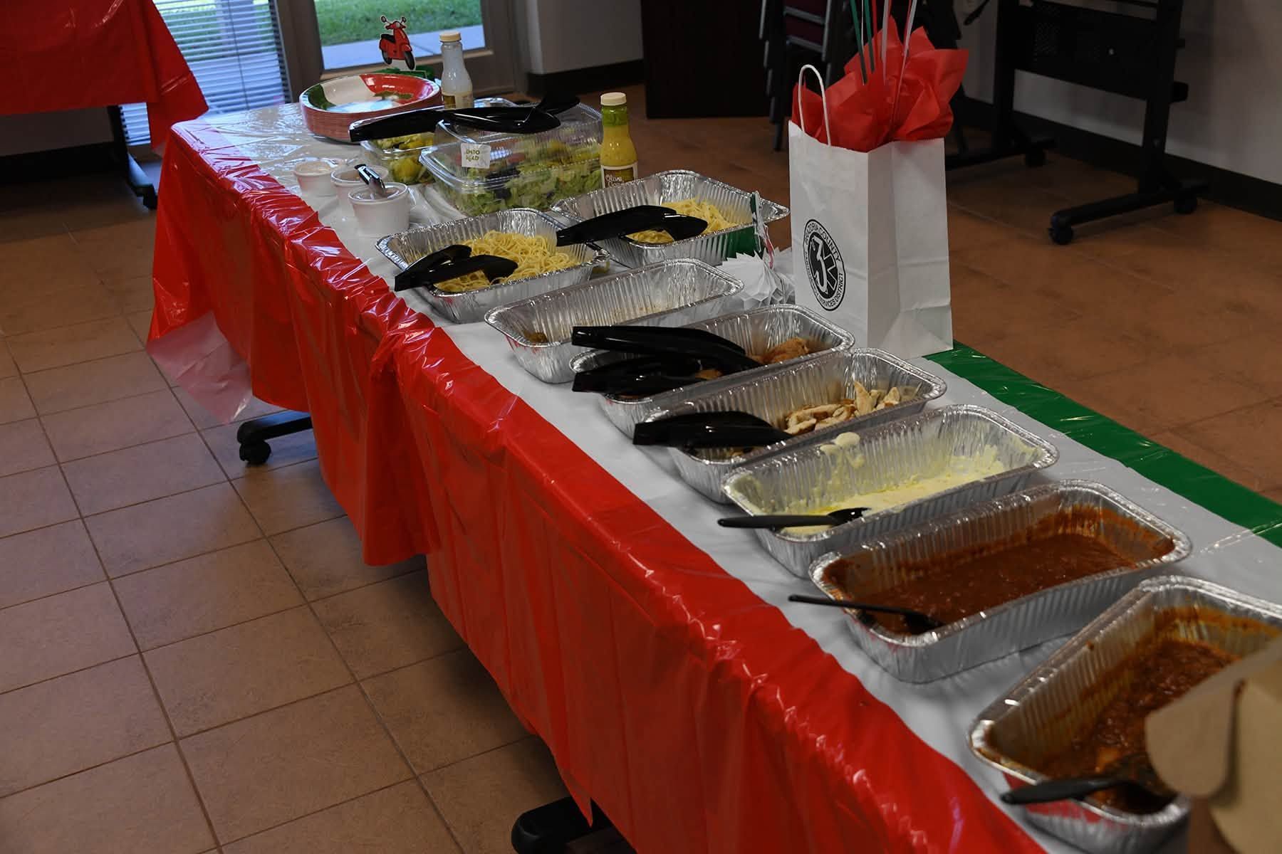 Buffet table with covered dishes and serving trays draped in red tablecloths in an indoor room