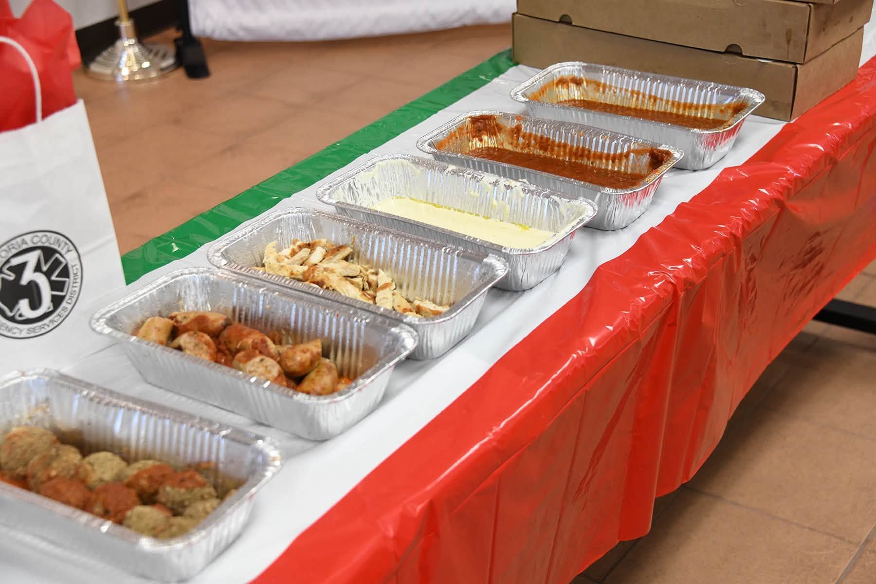 Foil trays of assorted food on a red tablecloth at a buffet table