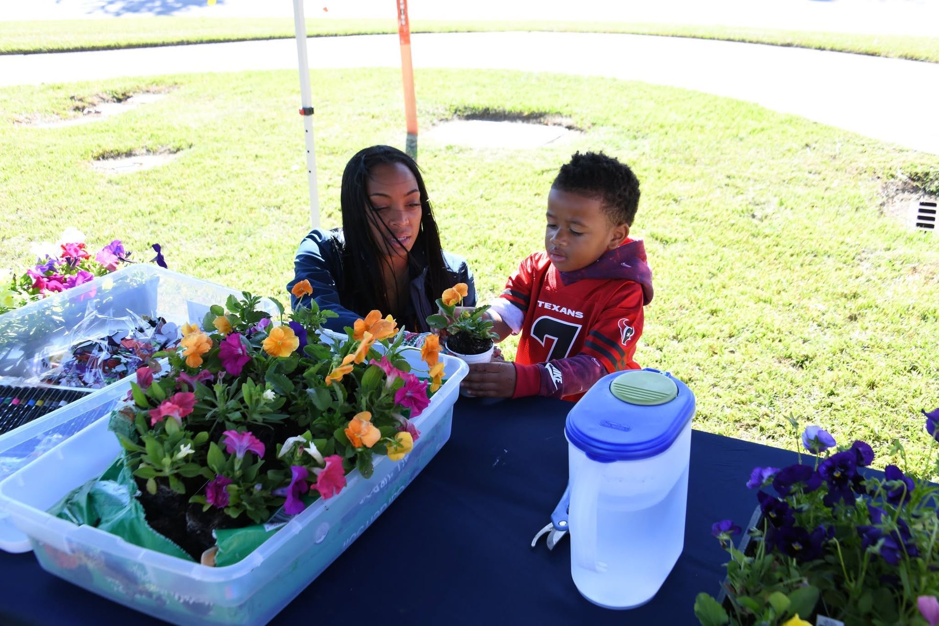 Two people tending colorful potted flowers at an outdoor table under a canopy