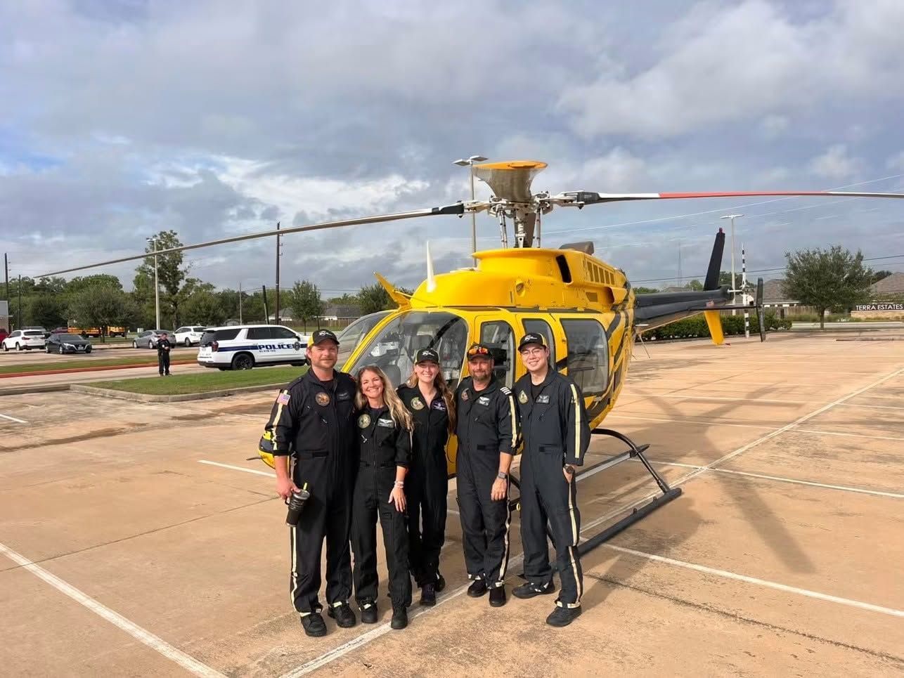 Five people in black uniforms stand in front of a yellow helicopter on a helipad.