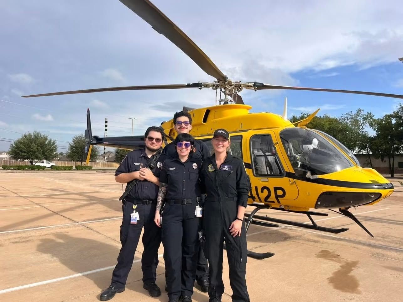 Four people in dark uniforms standing beside a yellow helicopter on a helipad