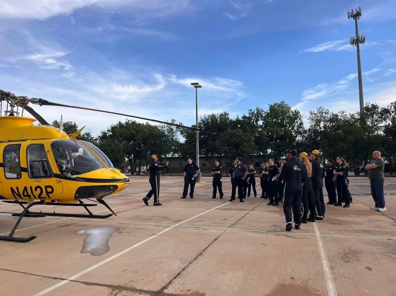 Yellow helicopter on a tarmac with a group of people standing nearby under a blue sky.