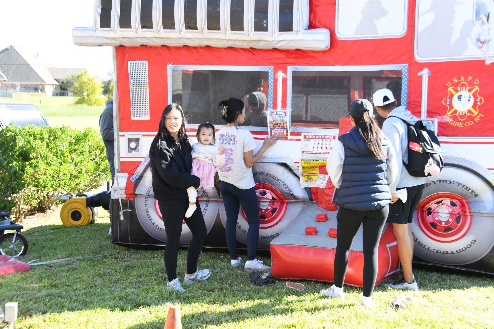 People posing beside a red-and-white fire truck bounce house on a sunny grassy field