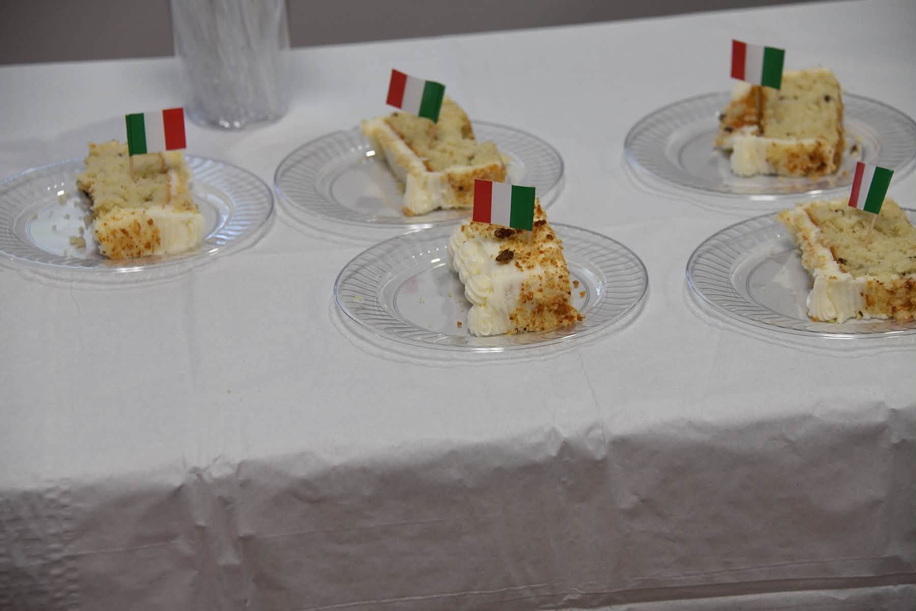 Small cake slices on clear plates with red, white, and green flags on a white tablecloth