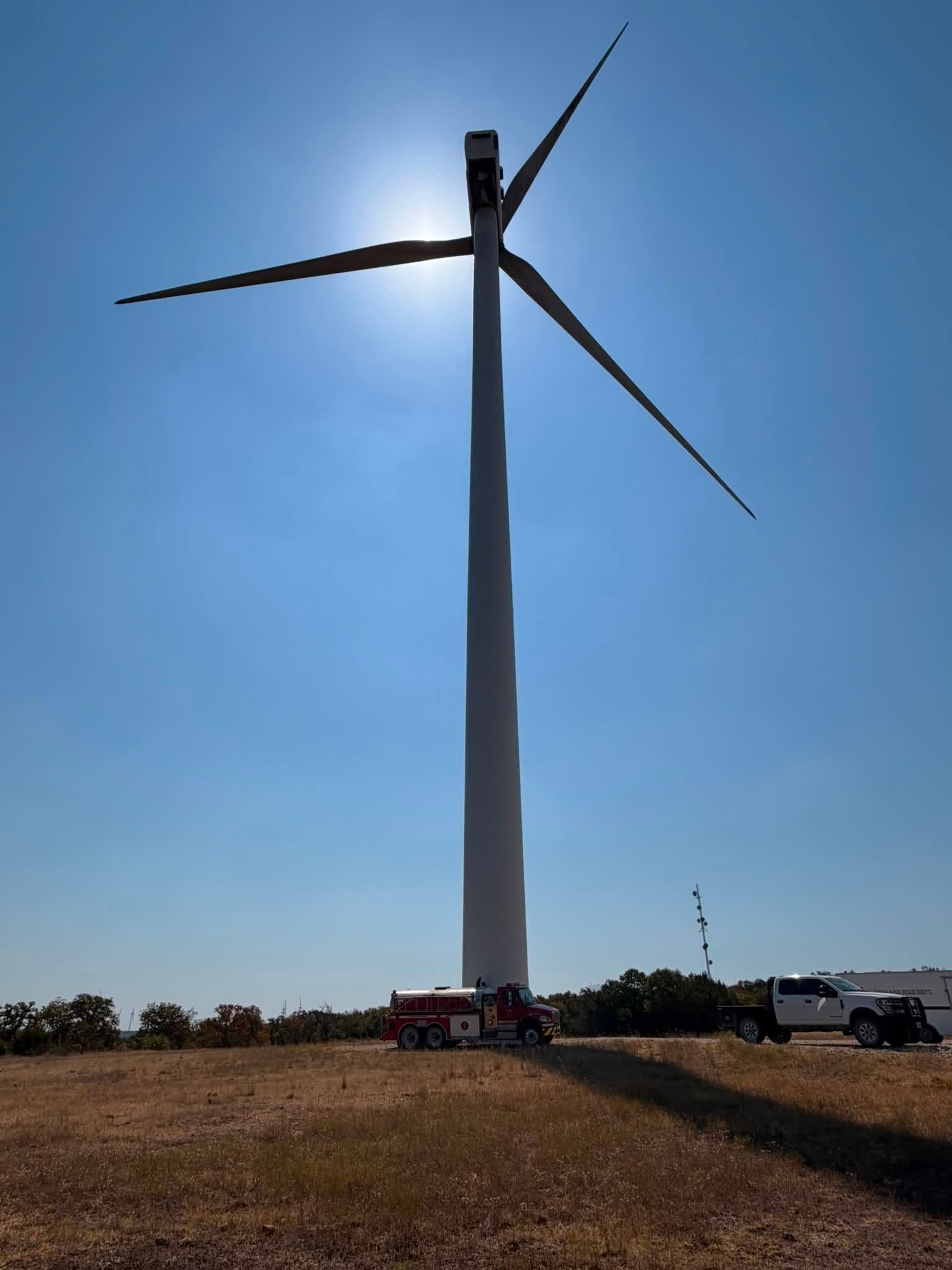 Wind turbine tower in a grassy field against a bright blue sky.