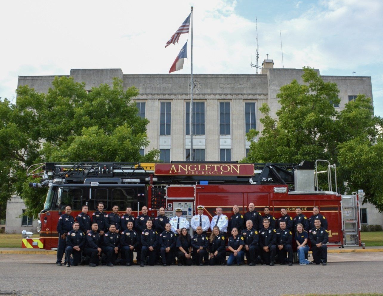 A group of firefighters are posing in front of an Angleton fire truck