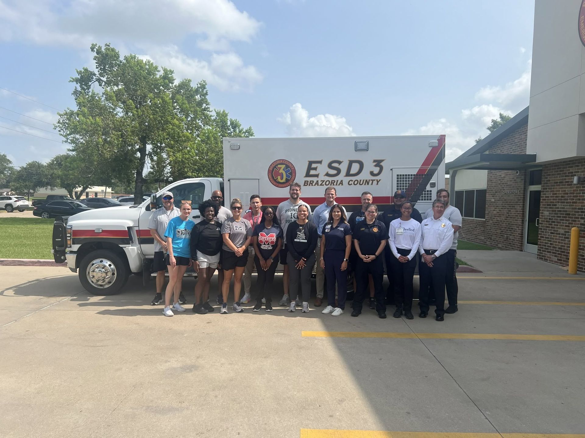 Group posing in front of an ESD3 truck and building, with emergency responders in uniform.