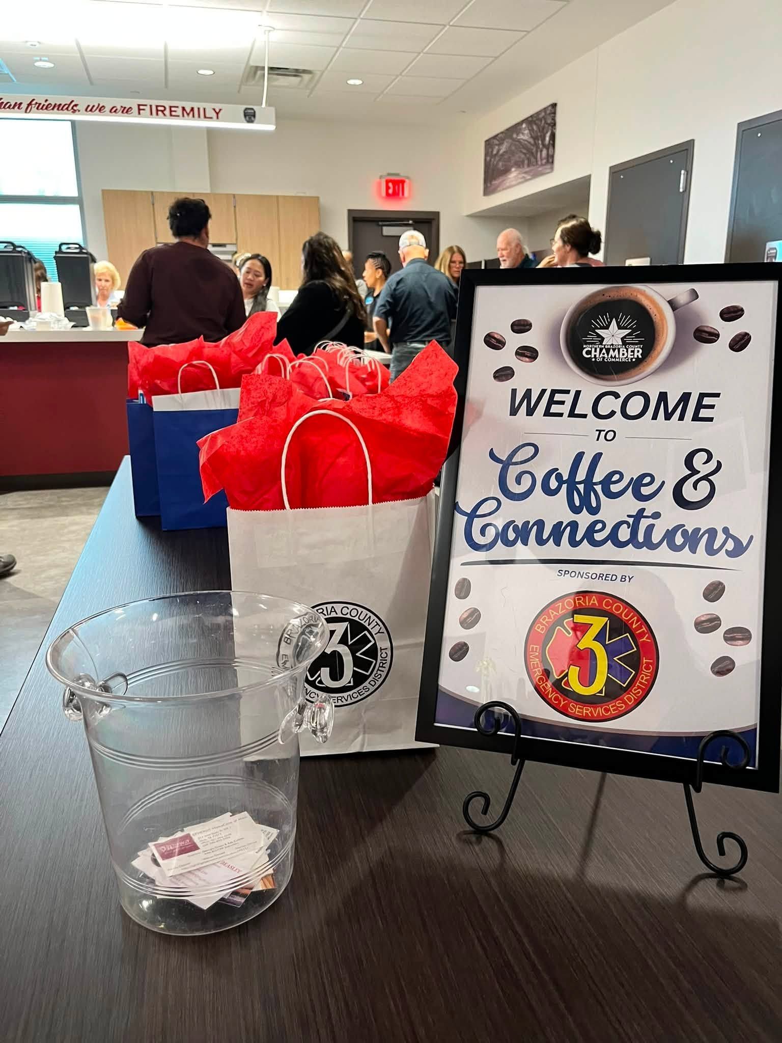 Welcome Coffee Connections sign beside a coffee cup and red gift bags at a community event table
