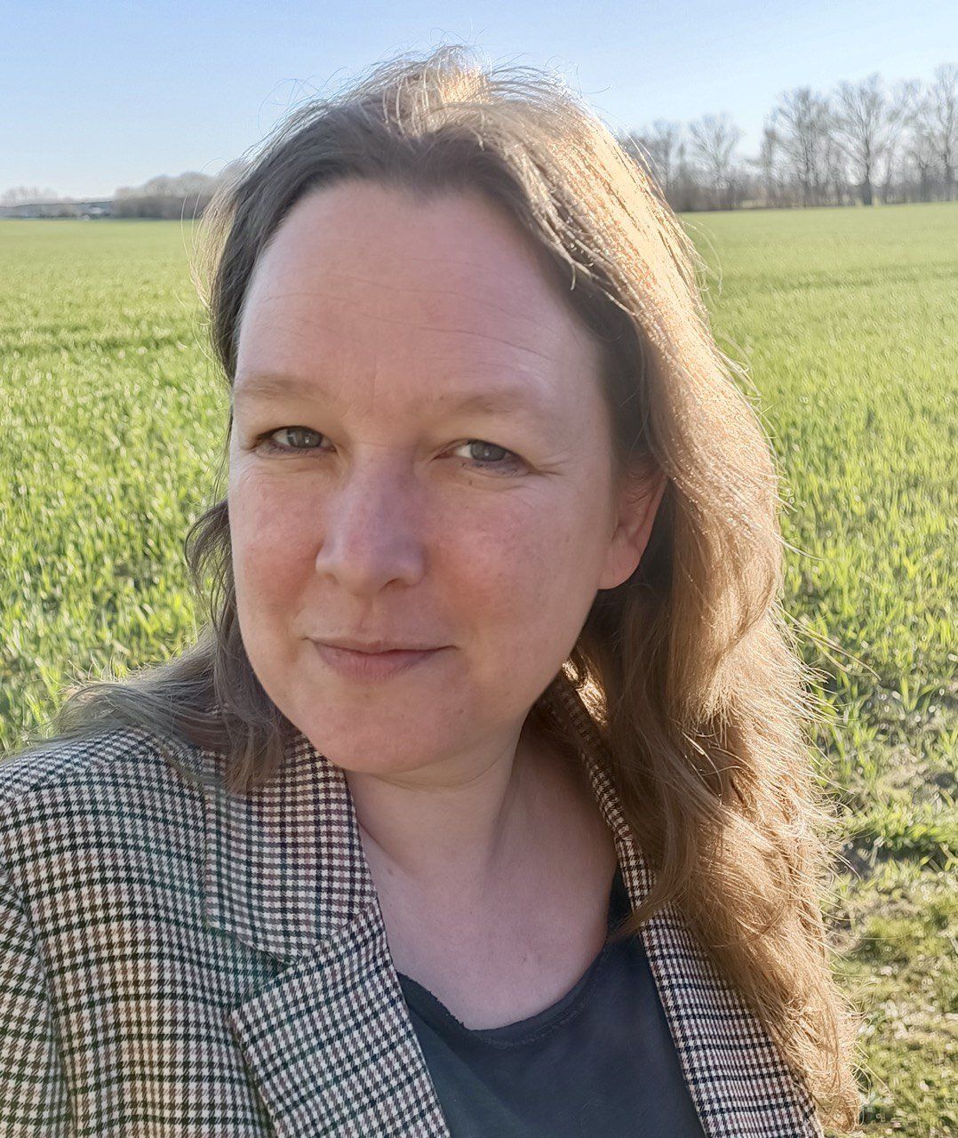 A woman in a plaid jacket is standing in a field.