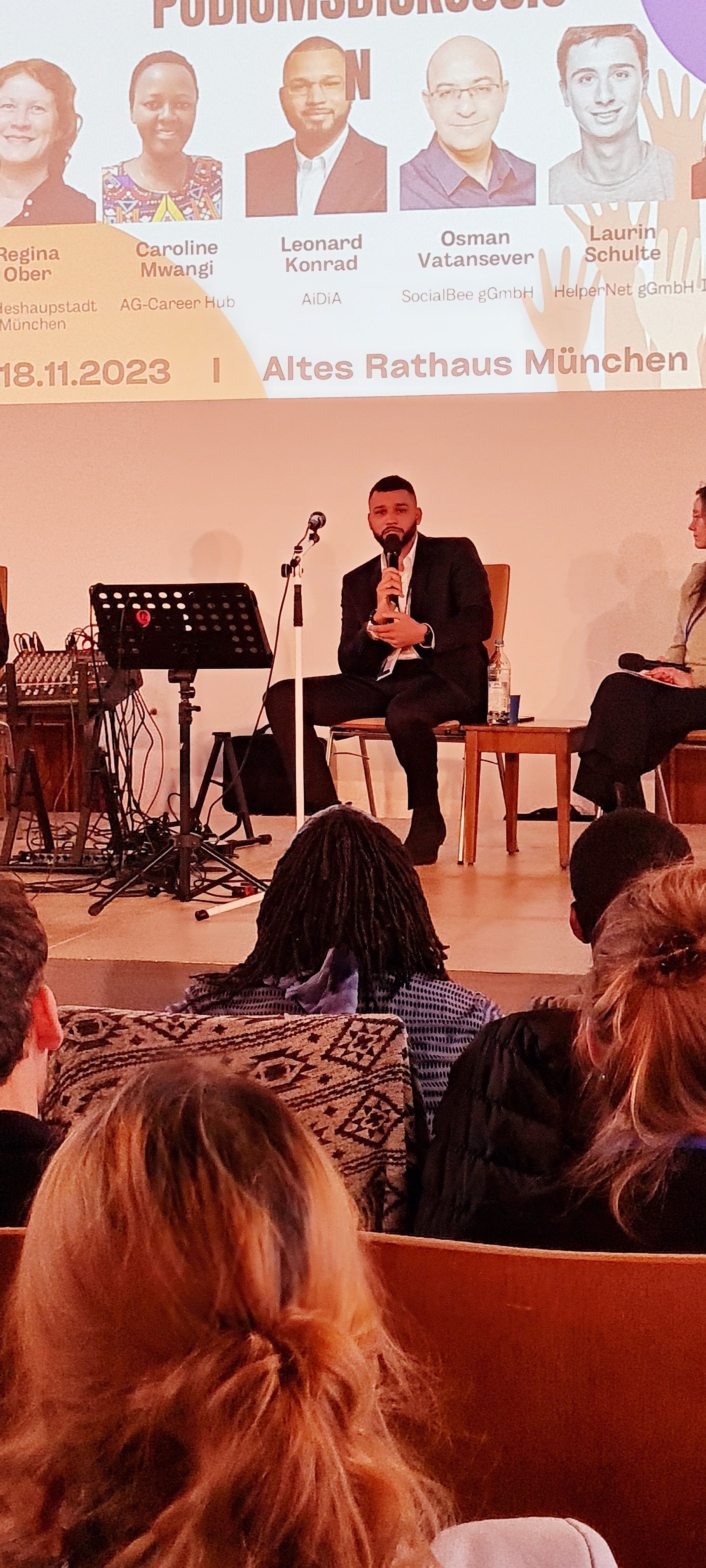 A man is sitting on a stage talking to a group of people.