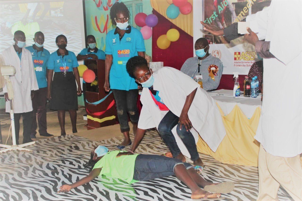 A group of people wearing masks are standing around a woman laying on the floor