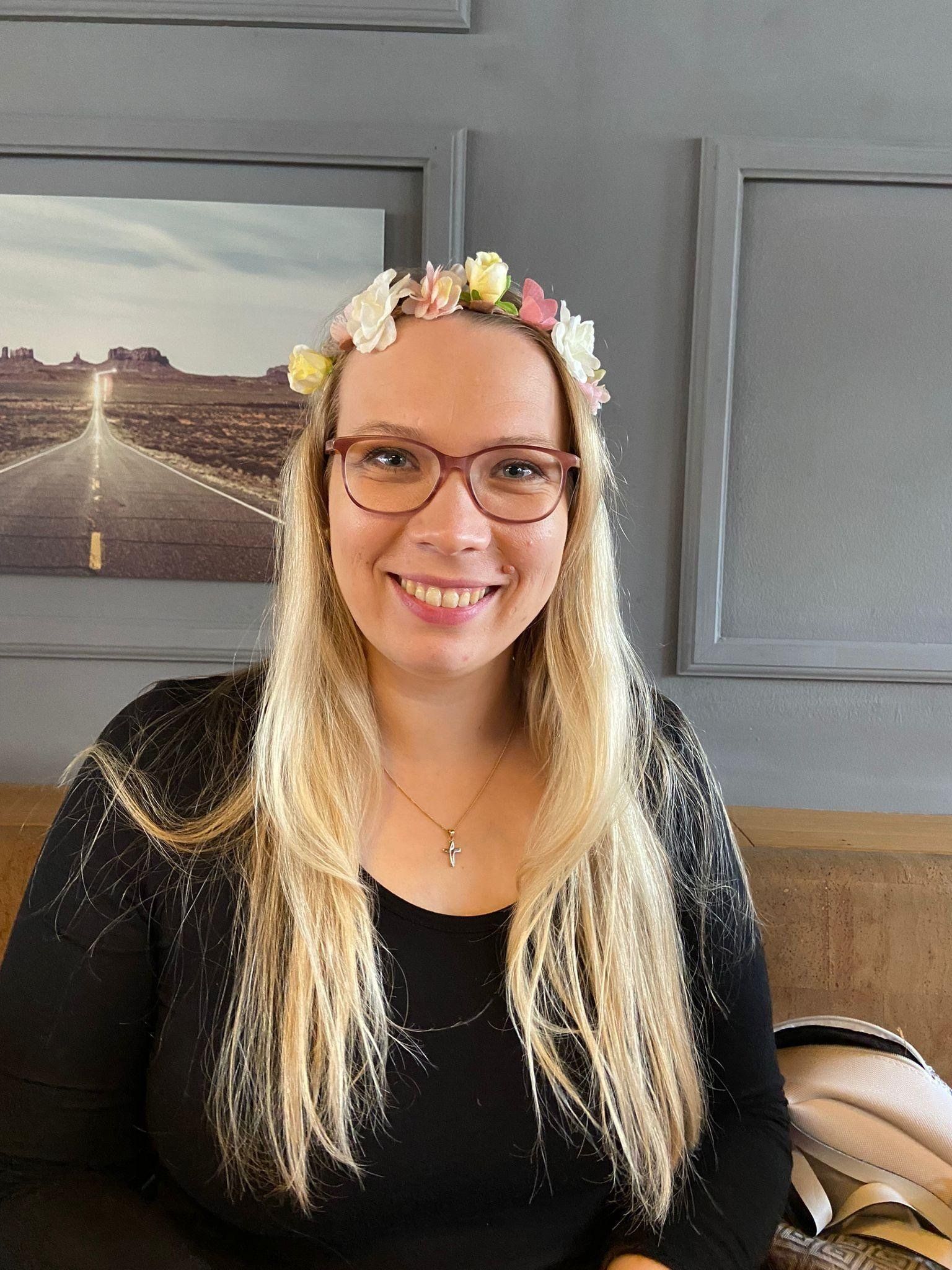 A woman wearing glasses and a flower crown is smiling for the camera.