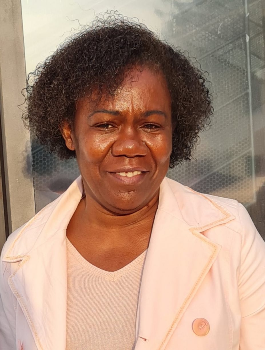 A woman with curly hair is wearing a pink jacket and smiling.