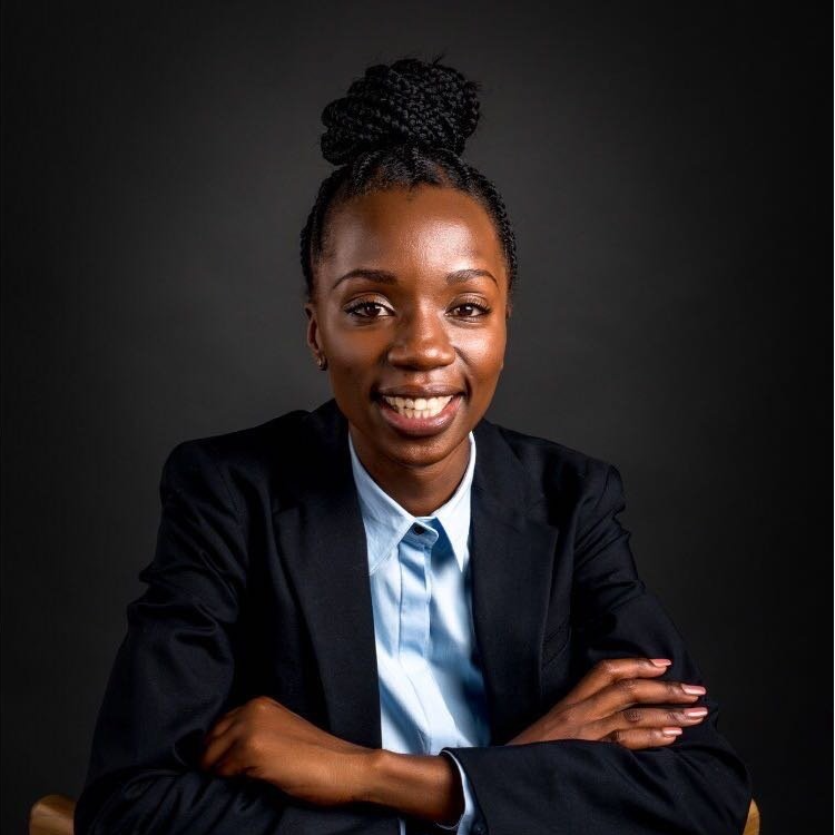 A woman in a suit and tie is sitting with her arms crossed and smiling.