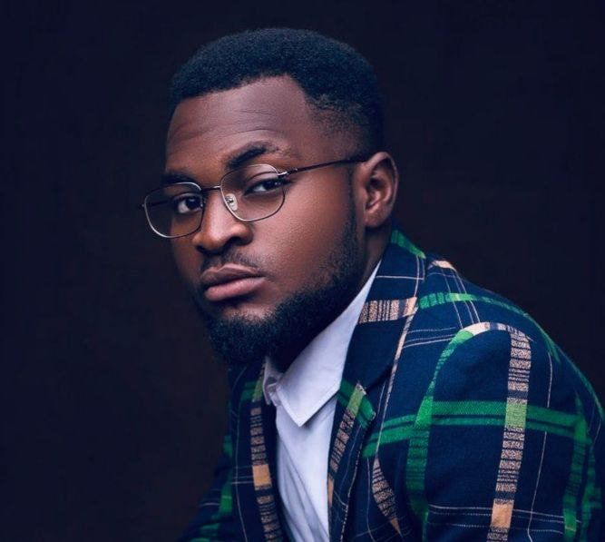 A man wearing glasses and a plaid jacket is looking at the camera.