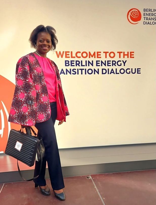 Woman in pink top and patterned jacket, holding a briefcase, at the Berlin Energy Transition Dialogue.