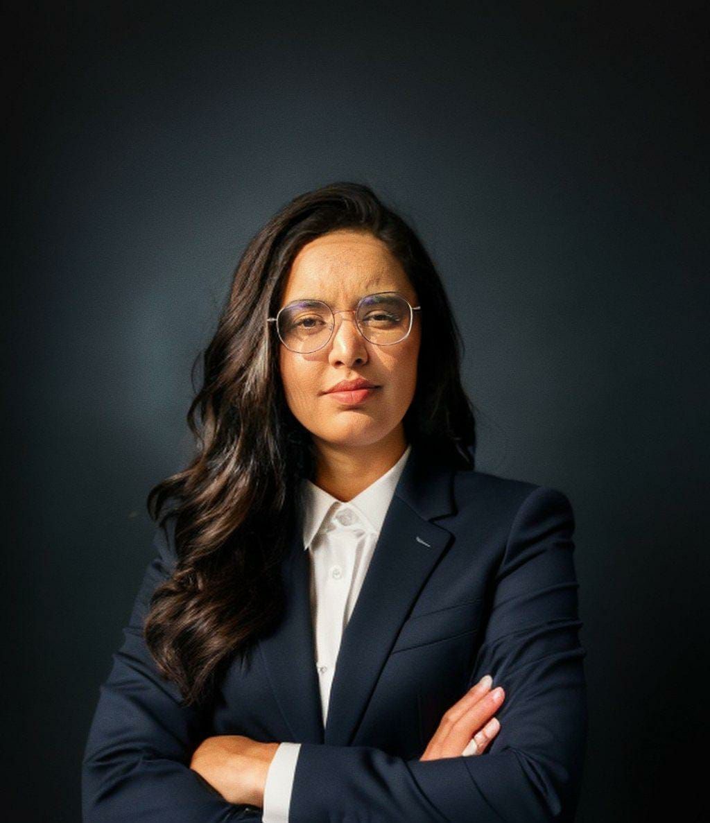 A woman in a suit and glasses is standing with her arms crossed.