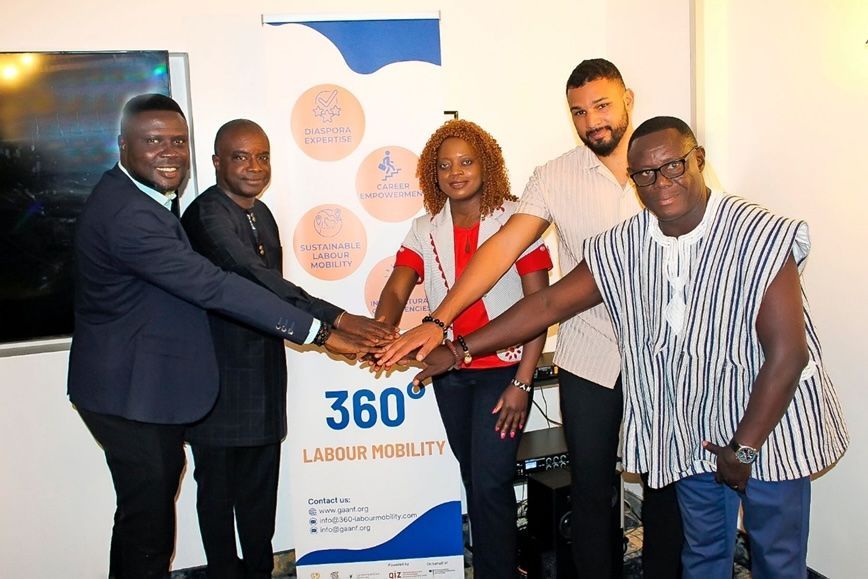 Five people stand together, stacking hands in front of a 360 Labour Mobility banner.