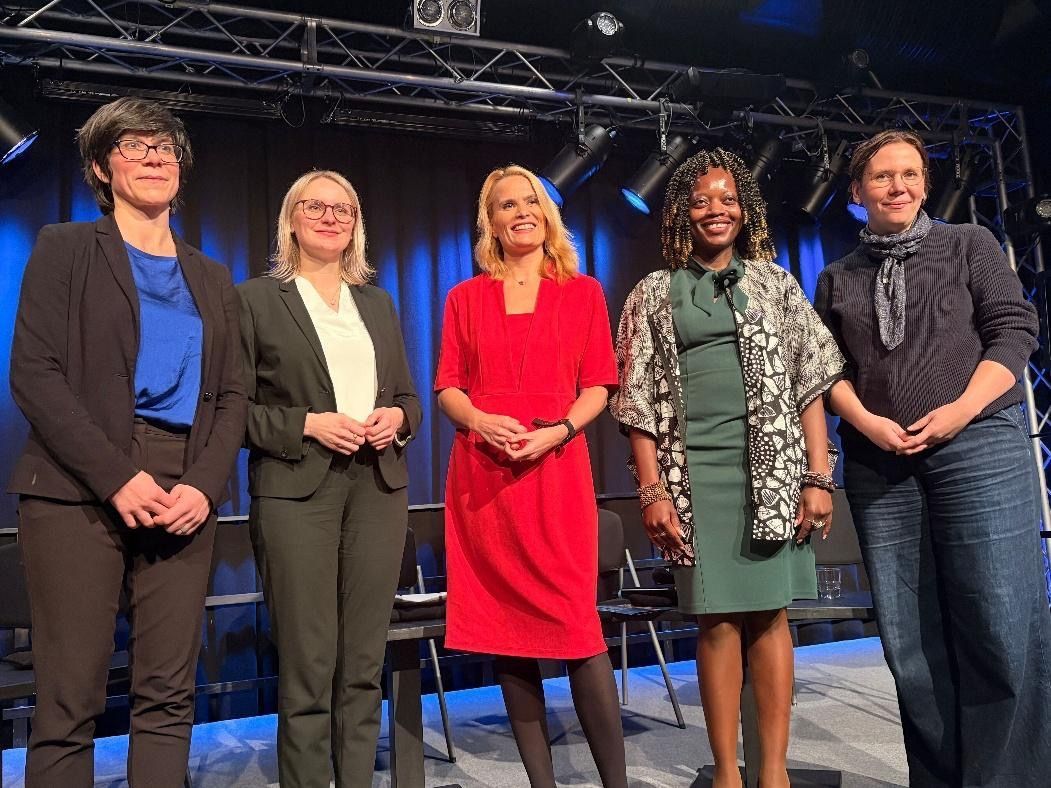 Five women standing onstage; a formal event.