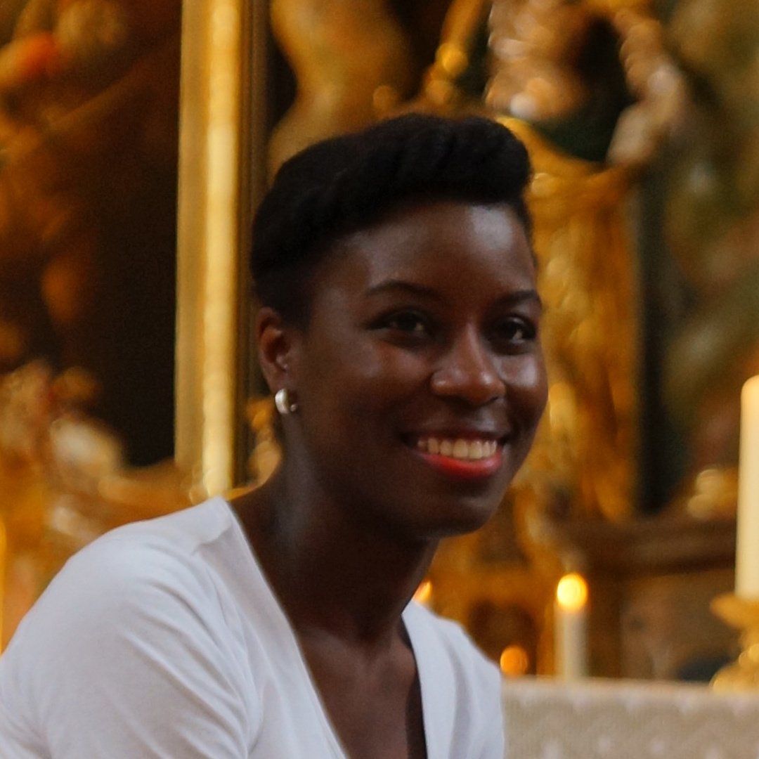 A woman in a white shirt is smiling in front of a painting