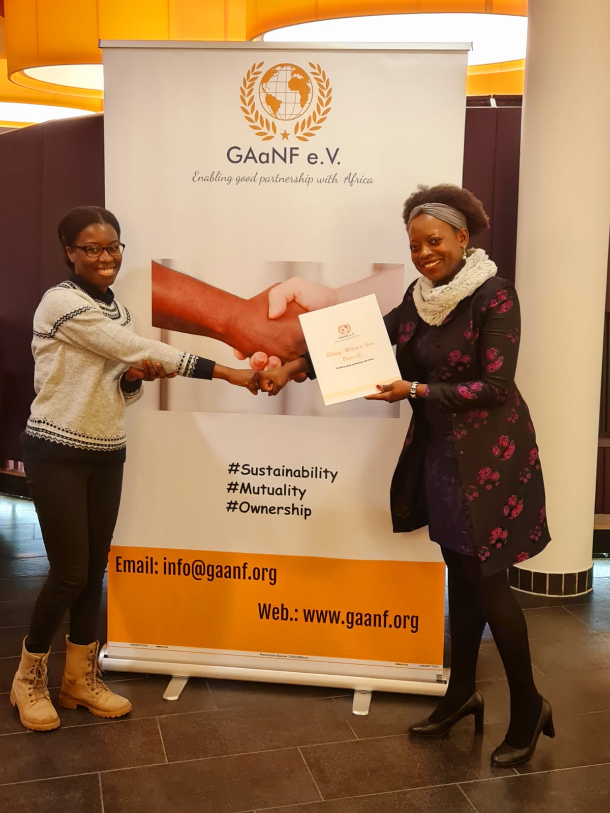 Two women shaking hands in front of a ganf banner