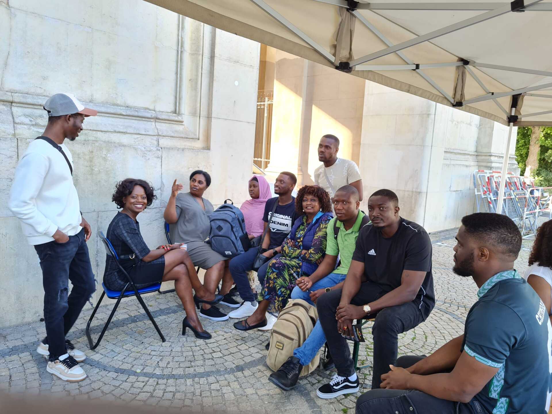 A group of people are sitting in chairs under an umbrella.