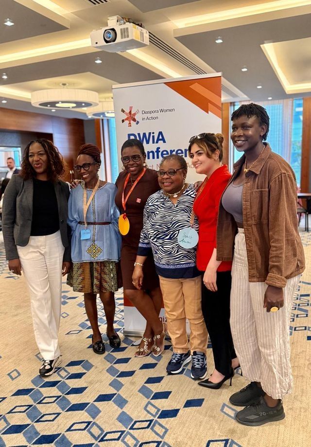 Group of six people posing for a photo at a conference with a logo.