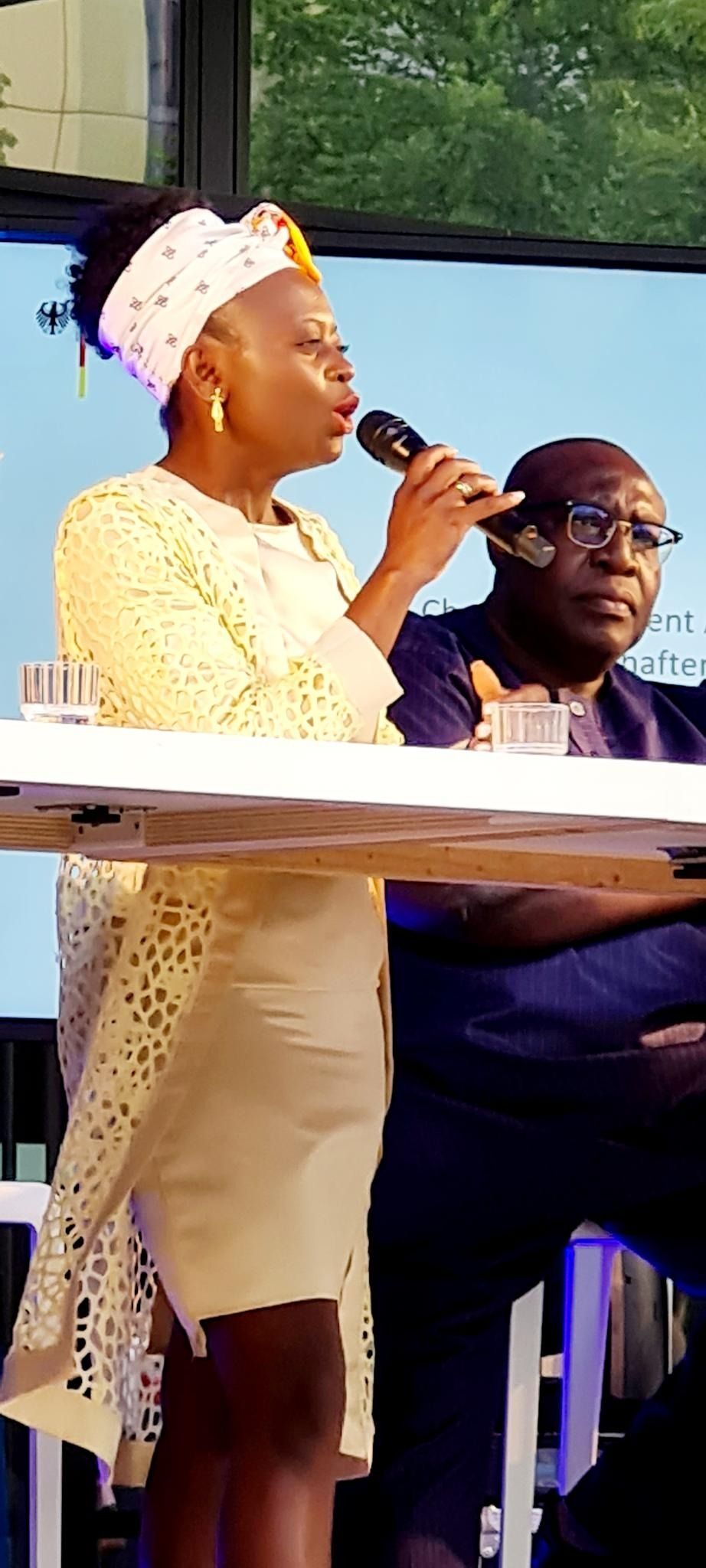 A woman is singing into a microphone while sitting at a table next to a man.