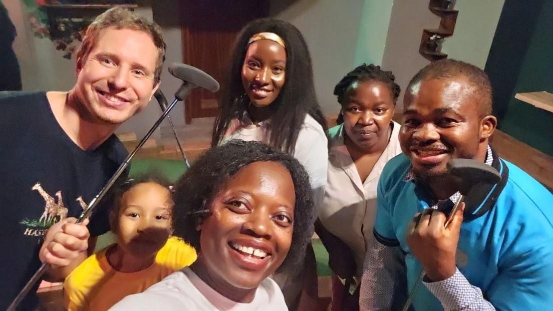 Group of people smiling at camera in a recording studio. Microphones visible.