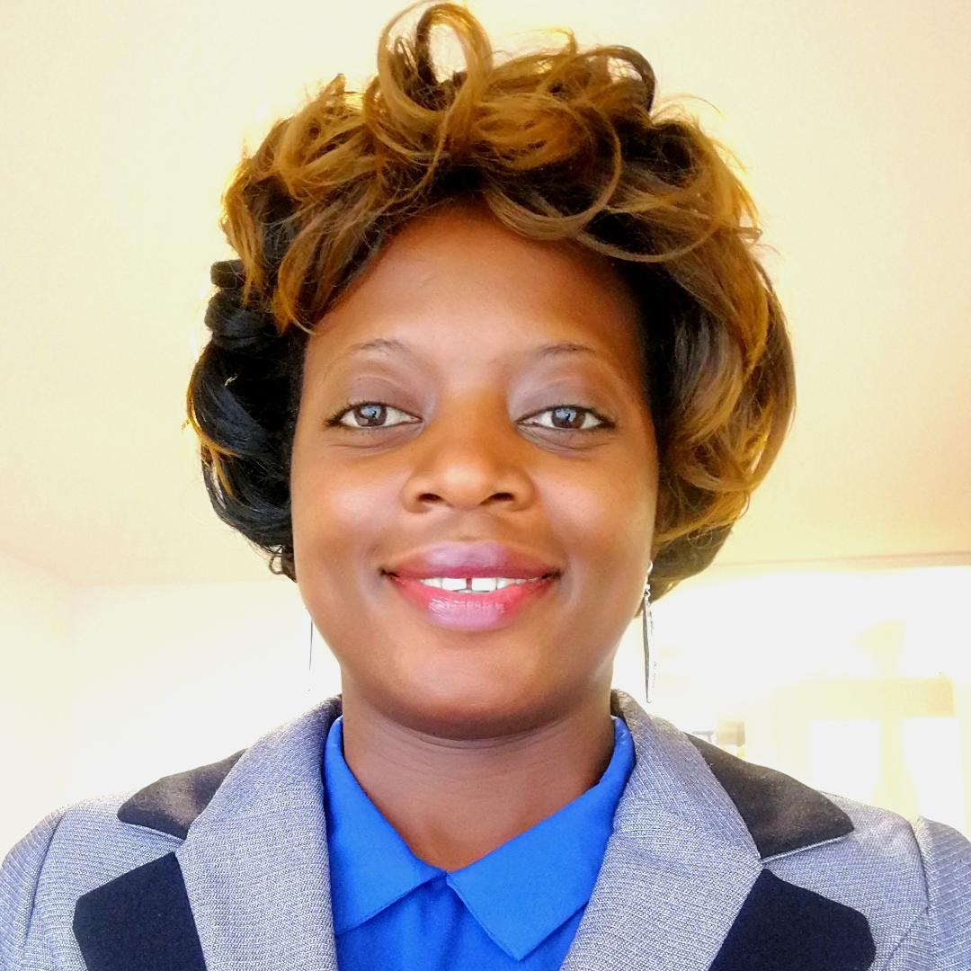 A woman wearing a blue shirt and a grey jacket smiles for the camera
