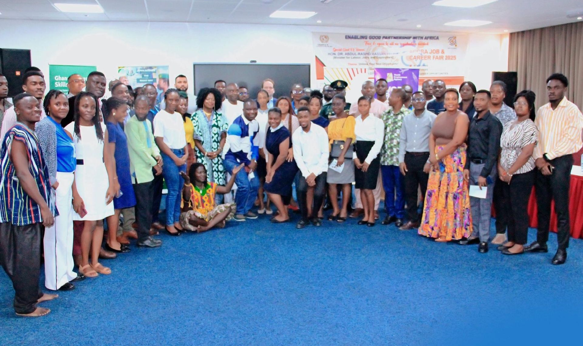 Large group posing indoors at an event, standing on a blue carpet in a brightly lit hall