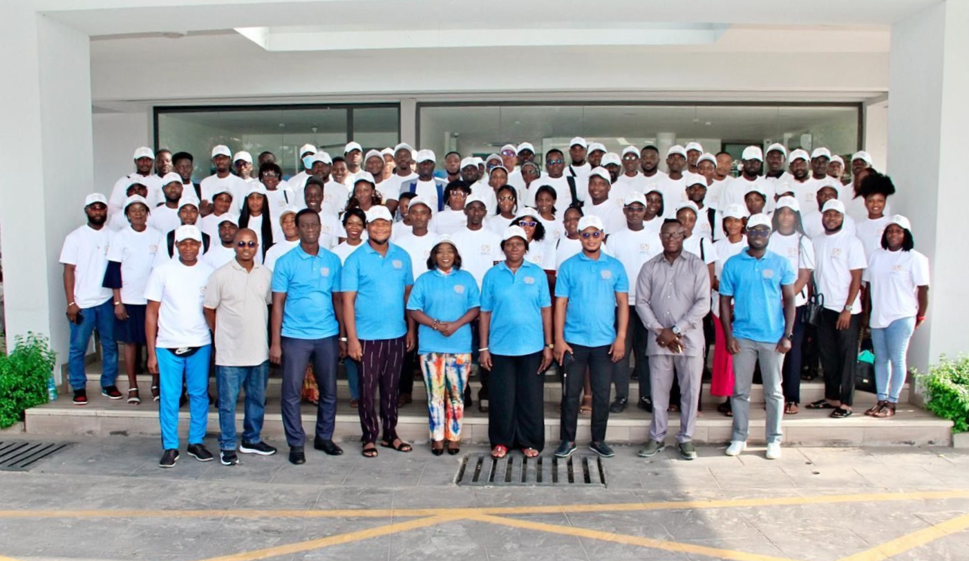 Large group posing in front of a building, some in white and blue shirts with a central podium arrangement