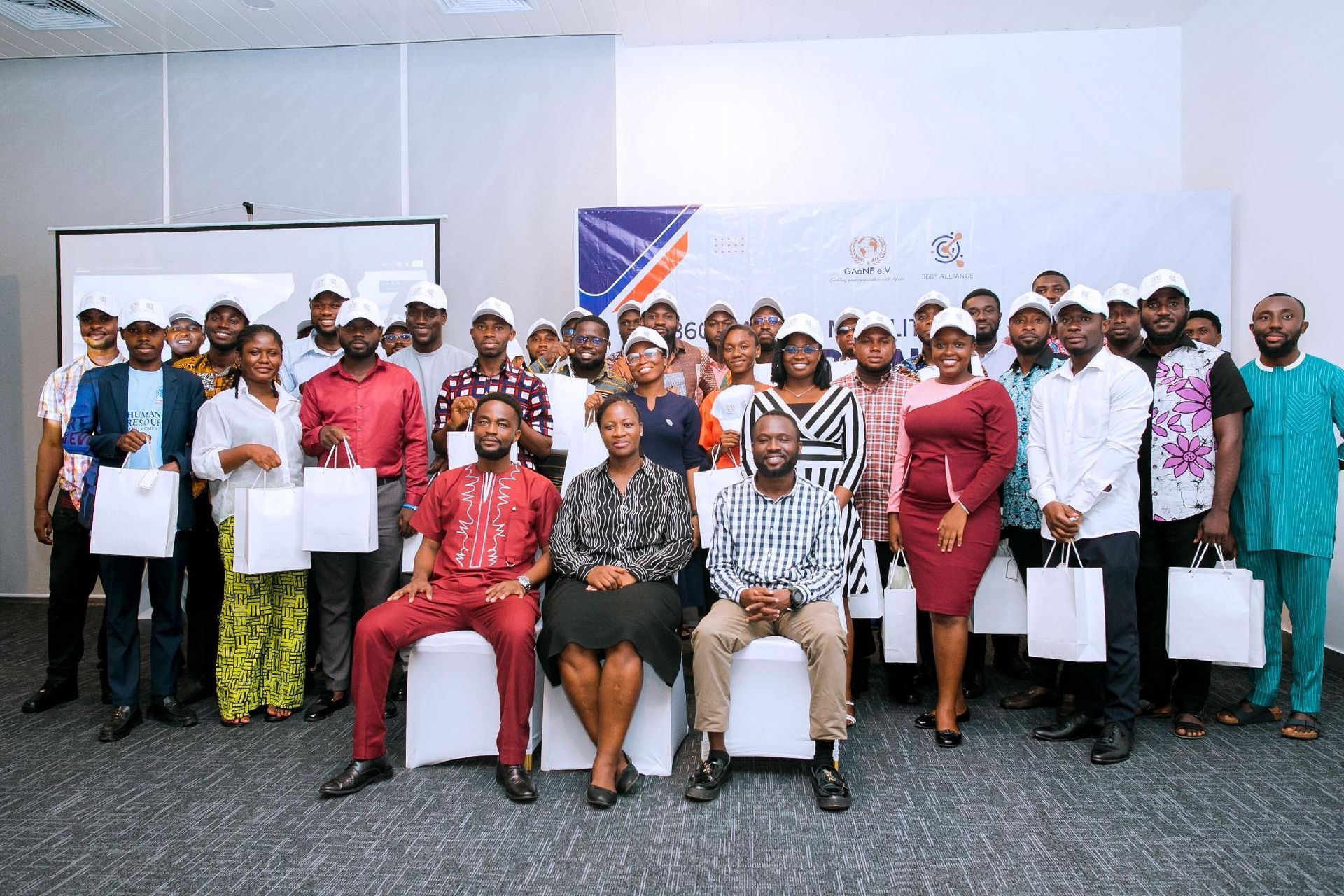 Group of people posing indoors at an event, some holding certificates, with a banner in the background.