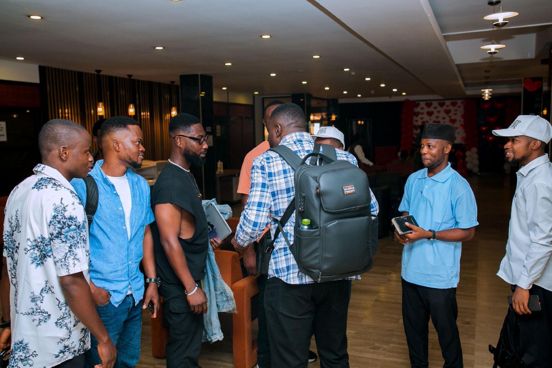 People standing and talking in a lobby, one person with a large backpack, others holding phones.