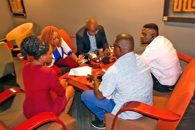 Five people meeting around a table in a lounge, with papers and a laptop on the table.