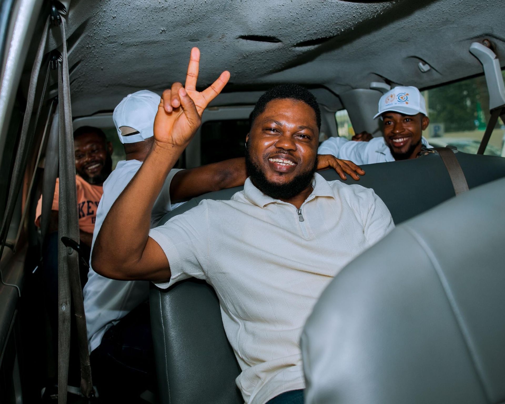 Three men smiling and posing in a car, one making a peace sign.