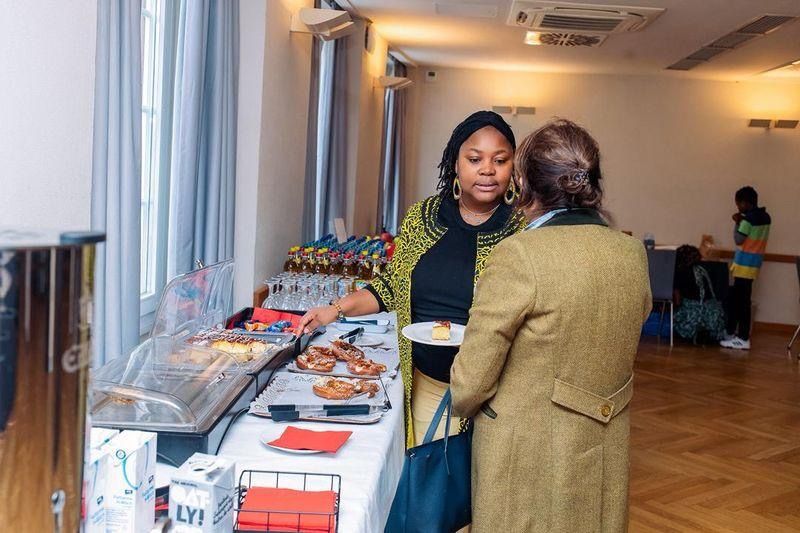Woman serving food to another person at a buffet table in a well-lit room.