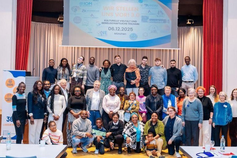 Group photo in front of a banner; diverse group smiles in a hall.