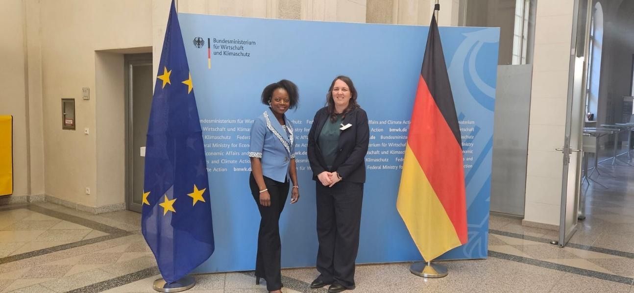 Two people standing in front of a blue backdrop with European Union and German flags.
