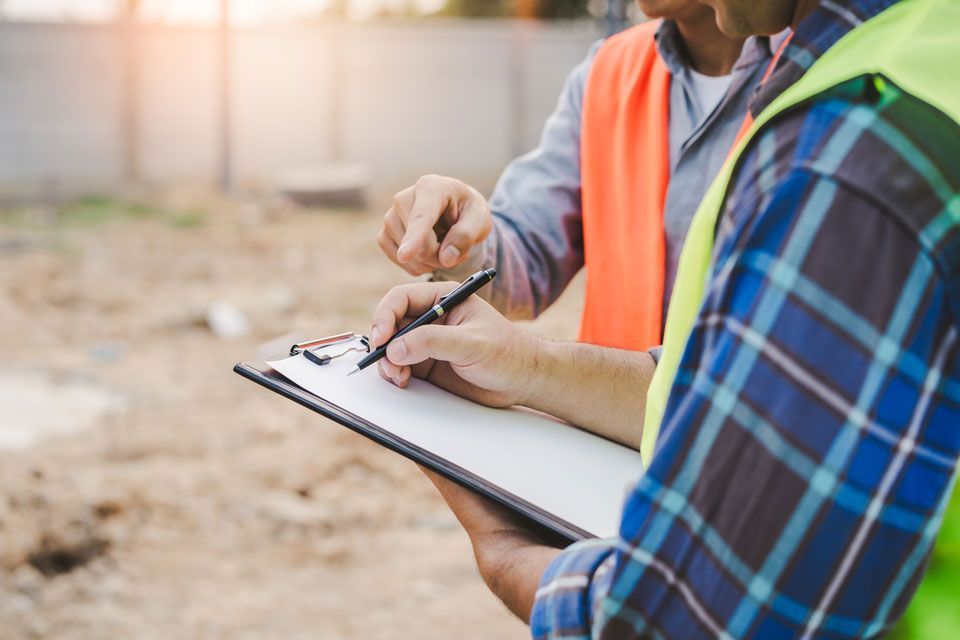 Two construction workers are looking at a clipboard on a construction site.