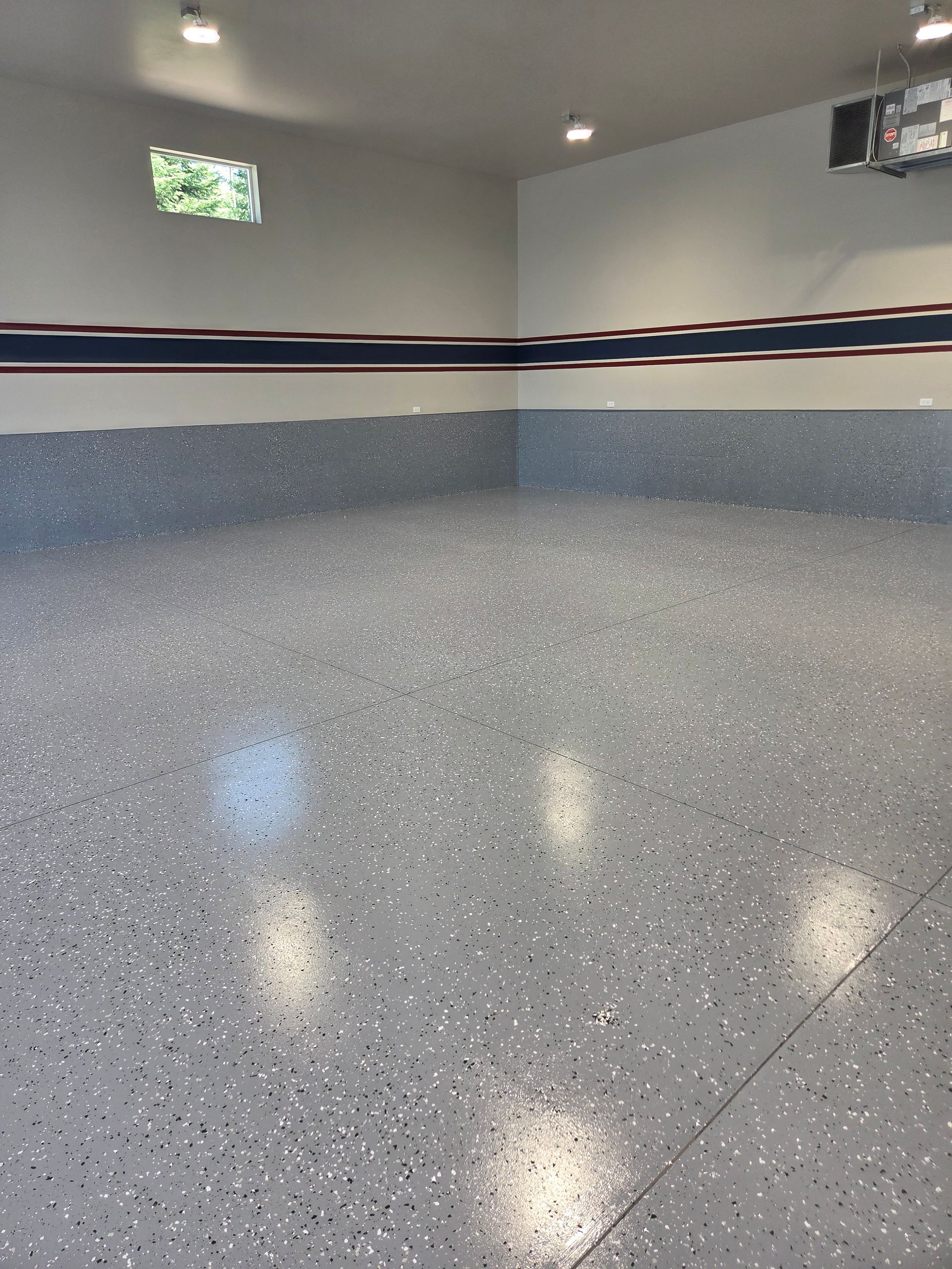 Empty polished garage with speckled gray floor and white walls, lit by ceiling lights.