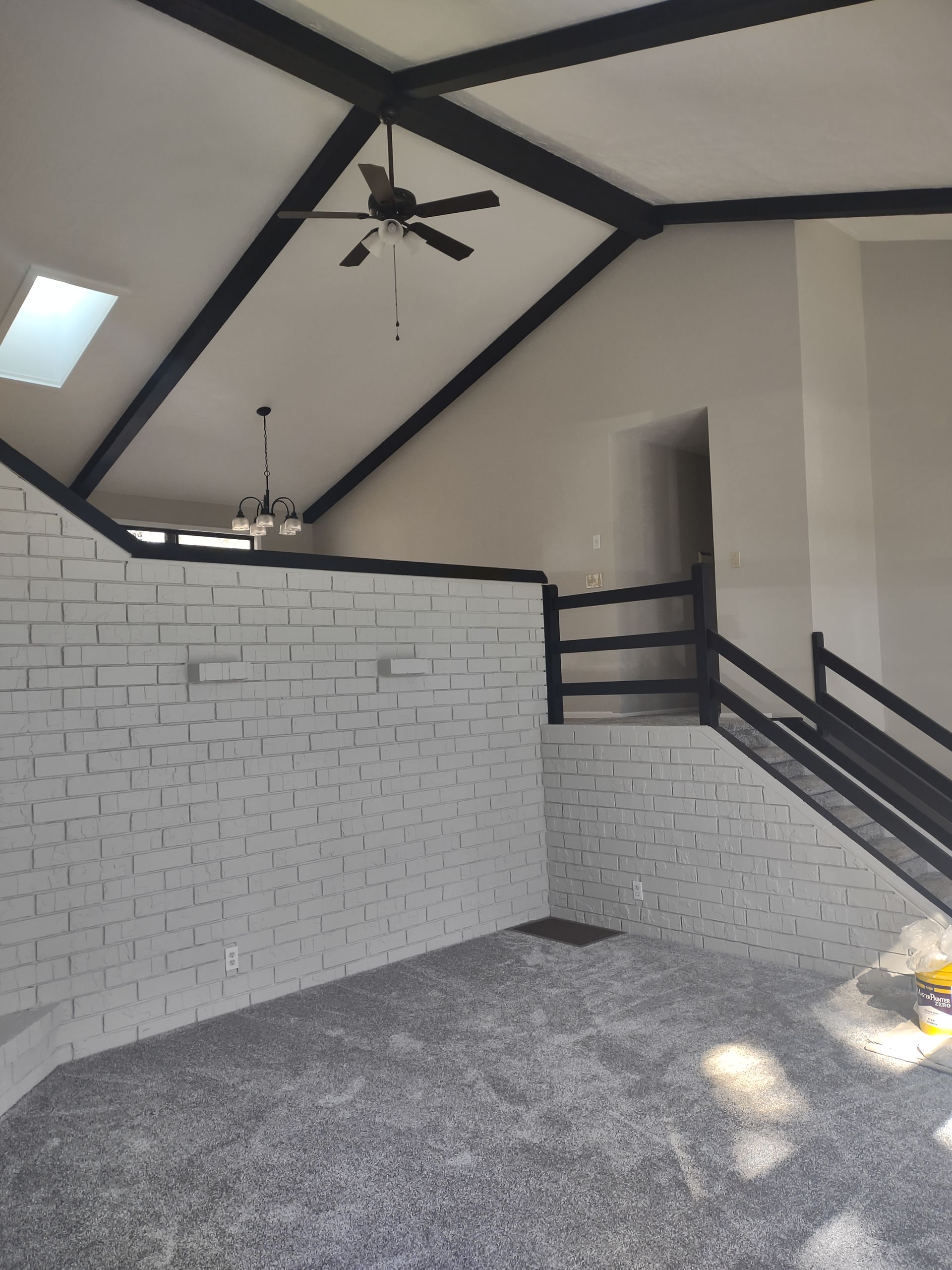 Interior of a modern loft with white brick wall, black railings, vaulted ceiling, and gray carpet.