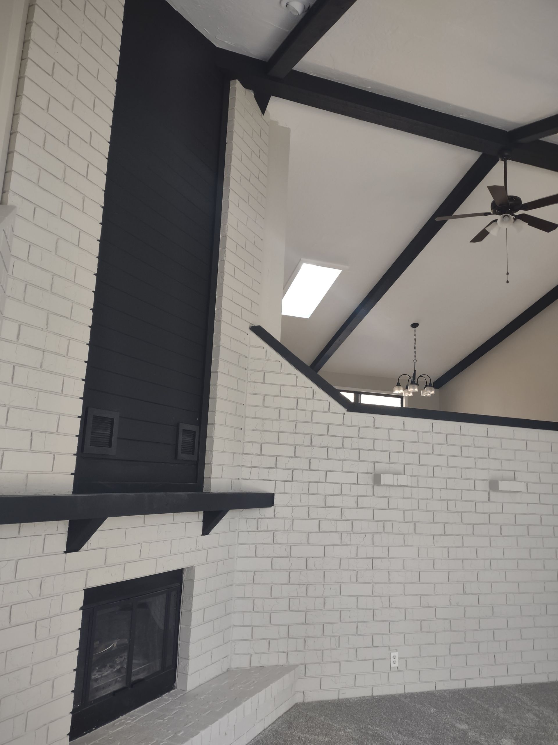 Modern room with white brick walls, black beams, ceiling fans, and a wall-mounted fireplace.
