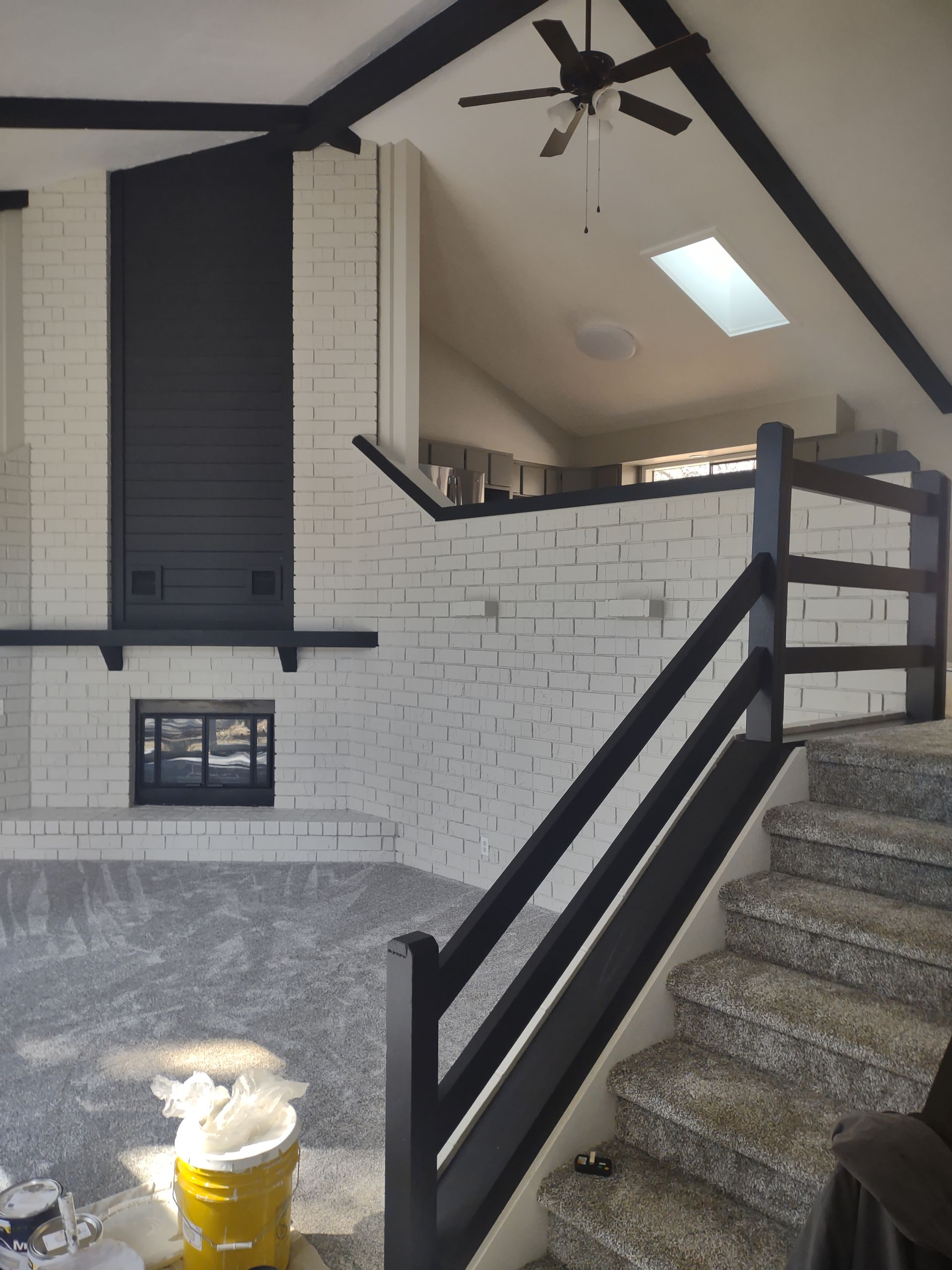 Covered porch with white brick walls, black railings, carpeted stairs, ceiling fan, and skylight.