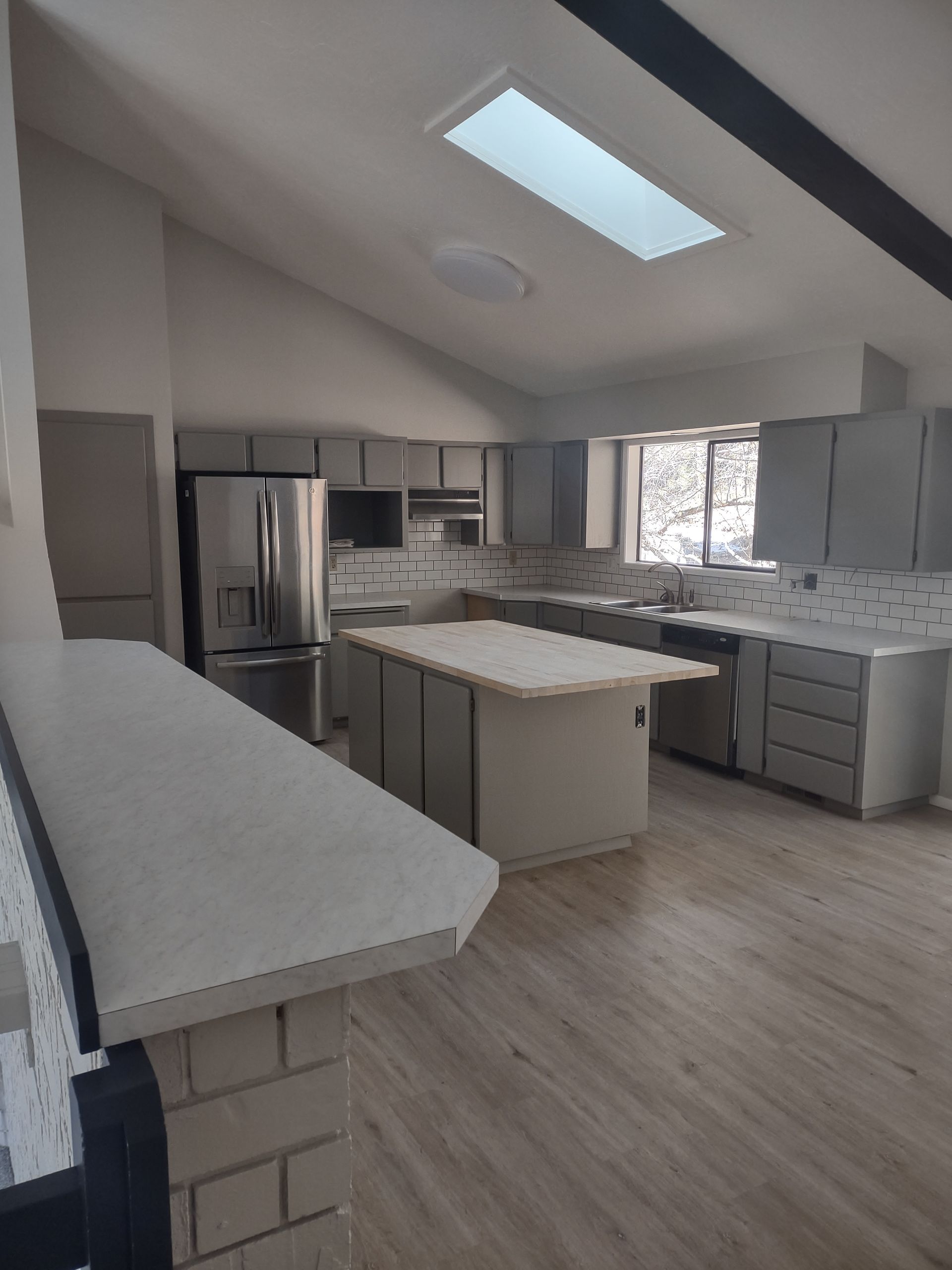 Bright modern kitchen with gray cabinets, stainless steel appliances, island, and skylight.