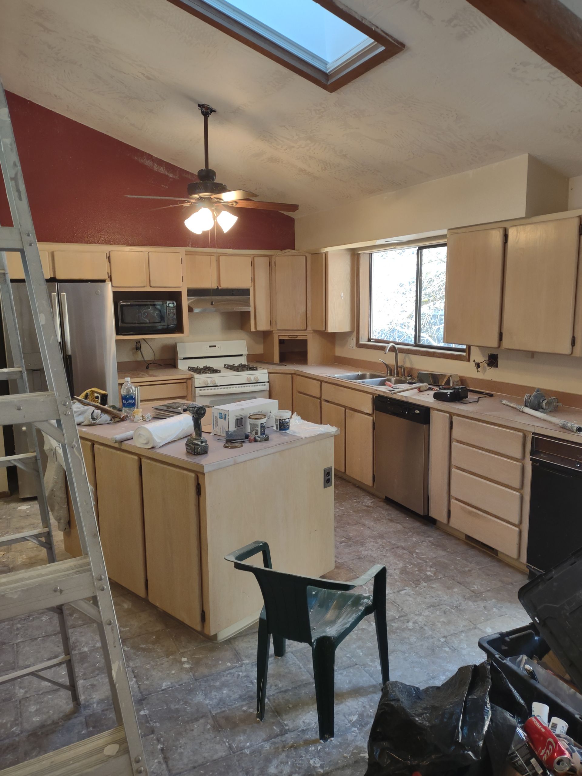 Kitchen under renovation with unfinished cabinets, scattered tools, and a ladder beneath a skylight.