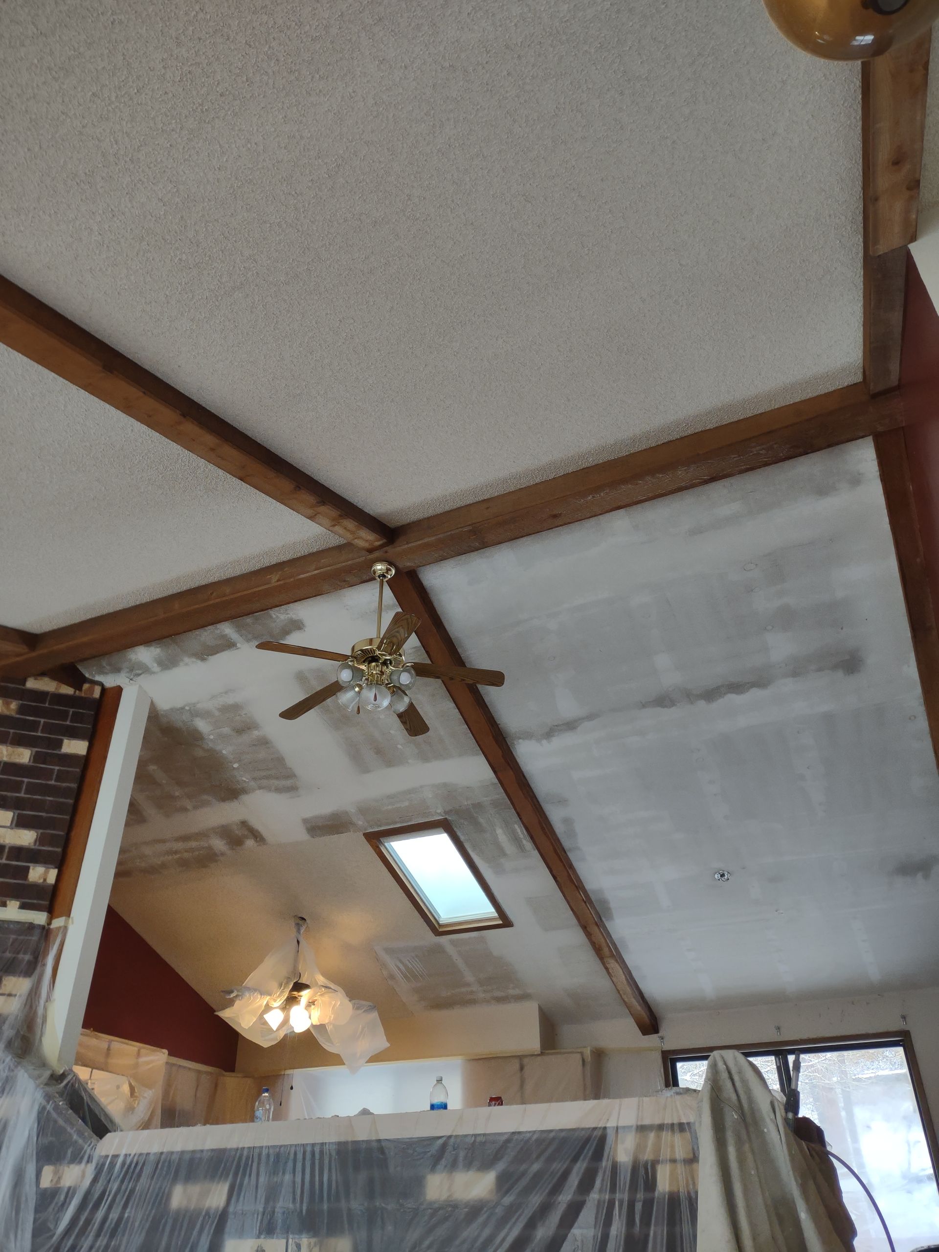 Ceiling with exposed wooden beams, ceiling fans, skylight, and track lighting in a room