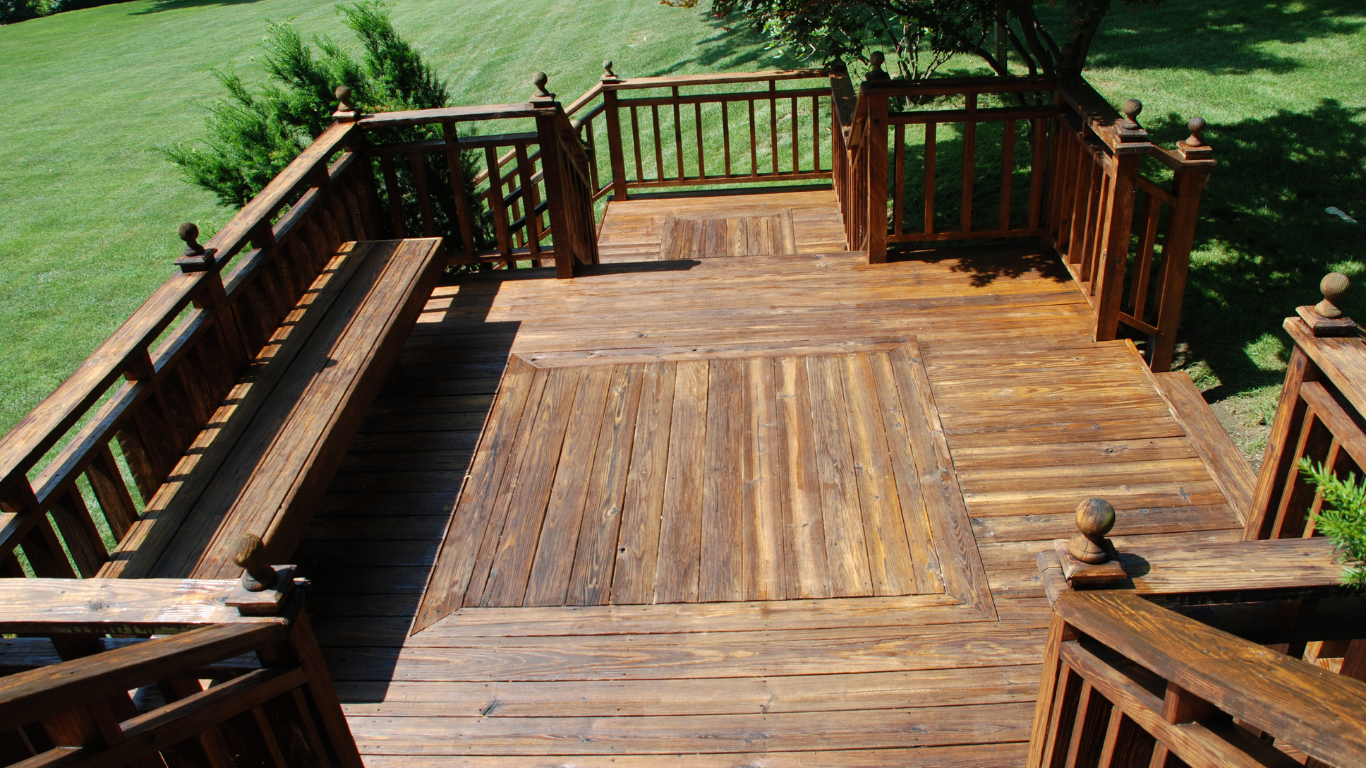 Wooden deck with benches and railings, overlooking a grassy yard in bright sunlight