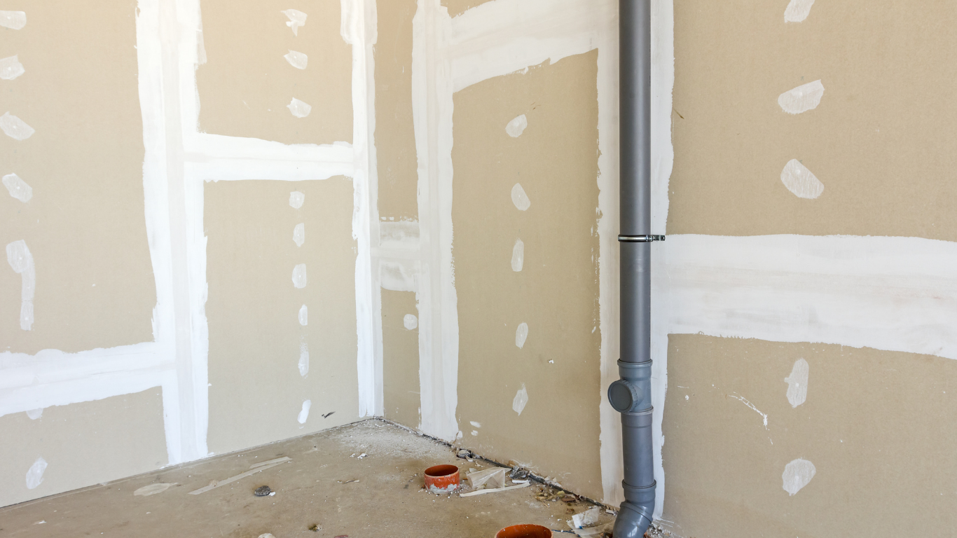 Unfinished room with beige drywall, white joint compound seams, and a gray pipe near the corner.